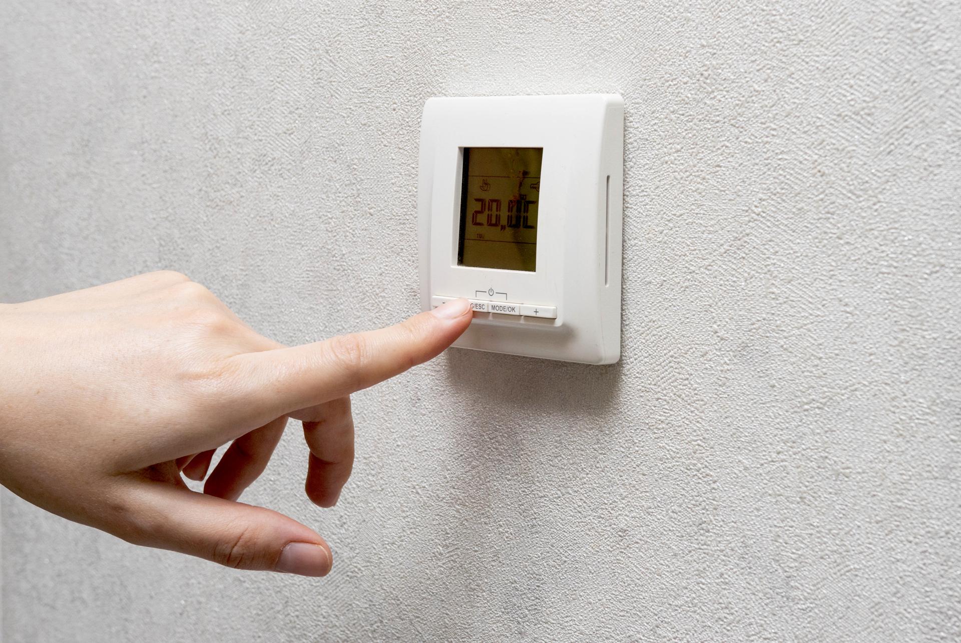 A person's hand presses the buttons on the smart home control wall sensor. Modern heating and cooling system of the house, comfortable temperature. Conditioning